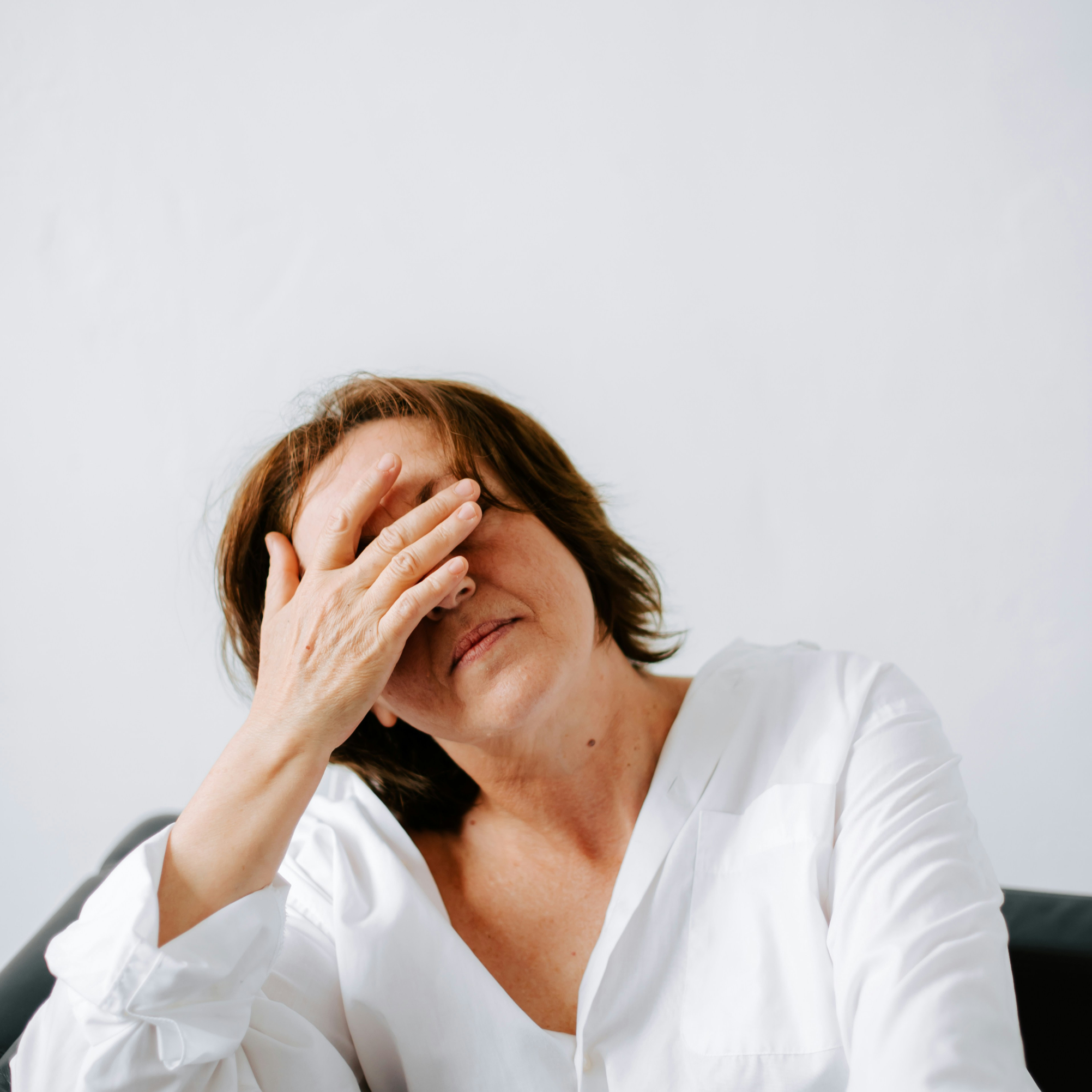A middle aged woman holds her head as she sits in an arm chair
